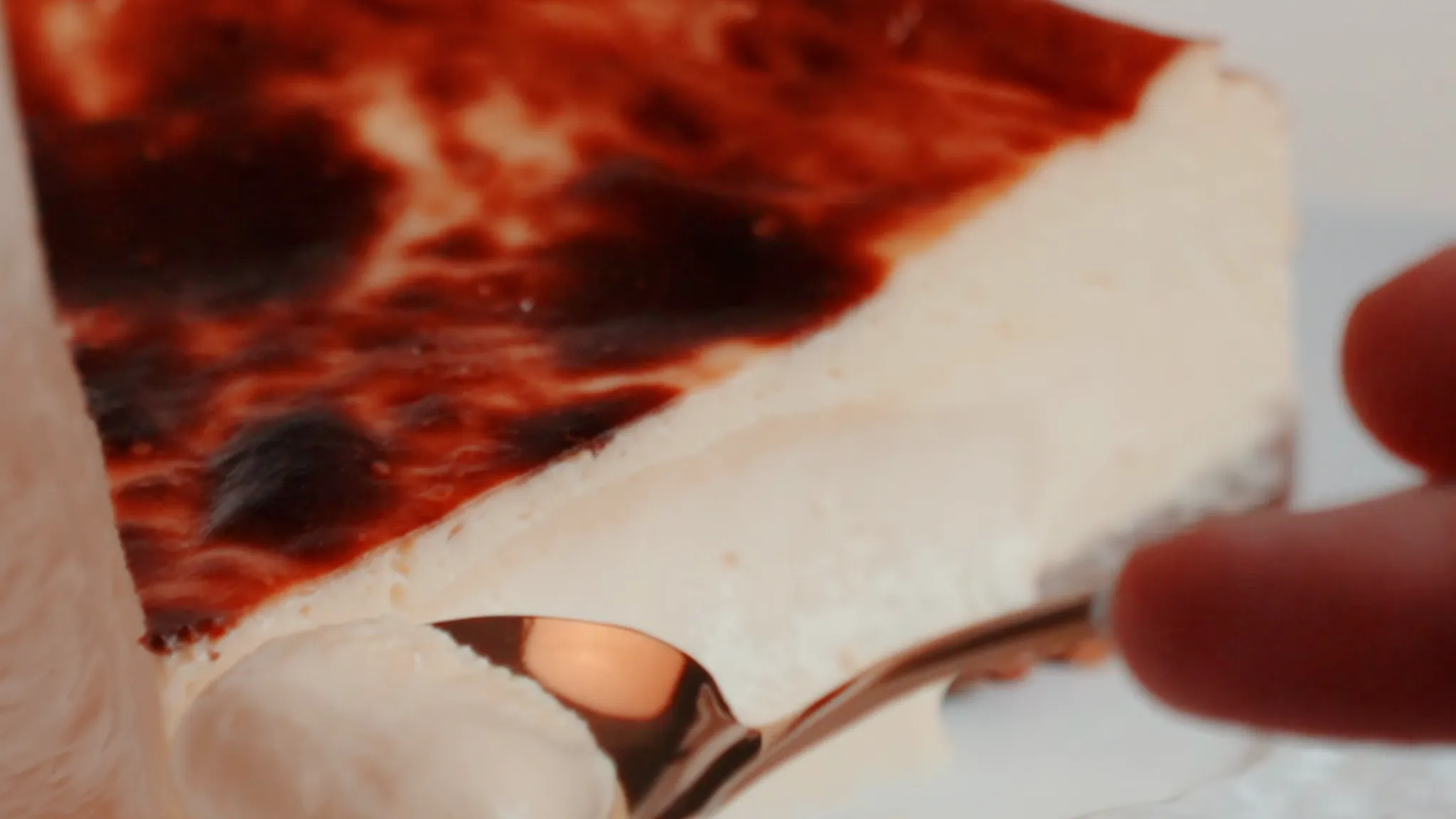 Spoon drawing a fold of soft cheese cream from a BasK Basque cheesecake, under the golden burnt top